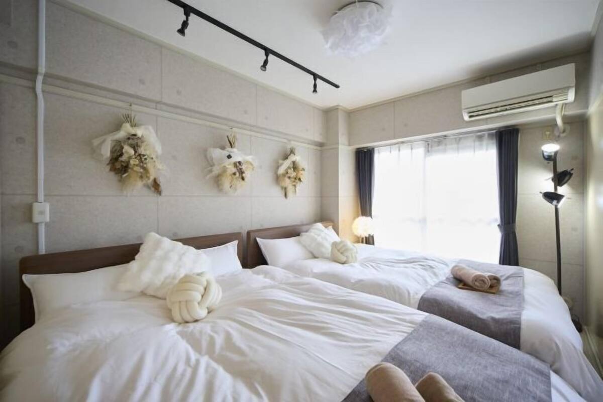 Une chambre d’hôtel avec deux lits, un climatiseur fixé au mur, un luminaire au plafond et une fenêtre avec des rideaux.