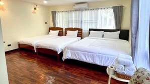 Camera d'albergo con due letti singoli e un letto matrimoniale, pavimento in legno, un tavolino con asciugamani e un condizionatore d'aria a parete.