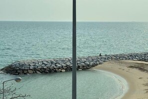Een kustgezicht met een rotsenrijke zeedijk, rustige zee en een zandstrand.