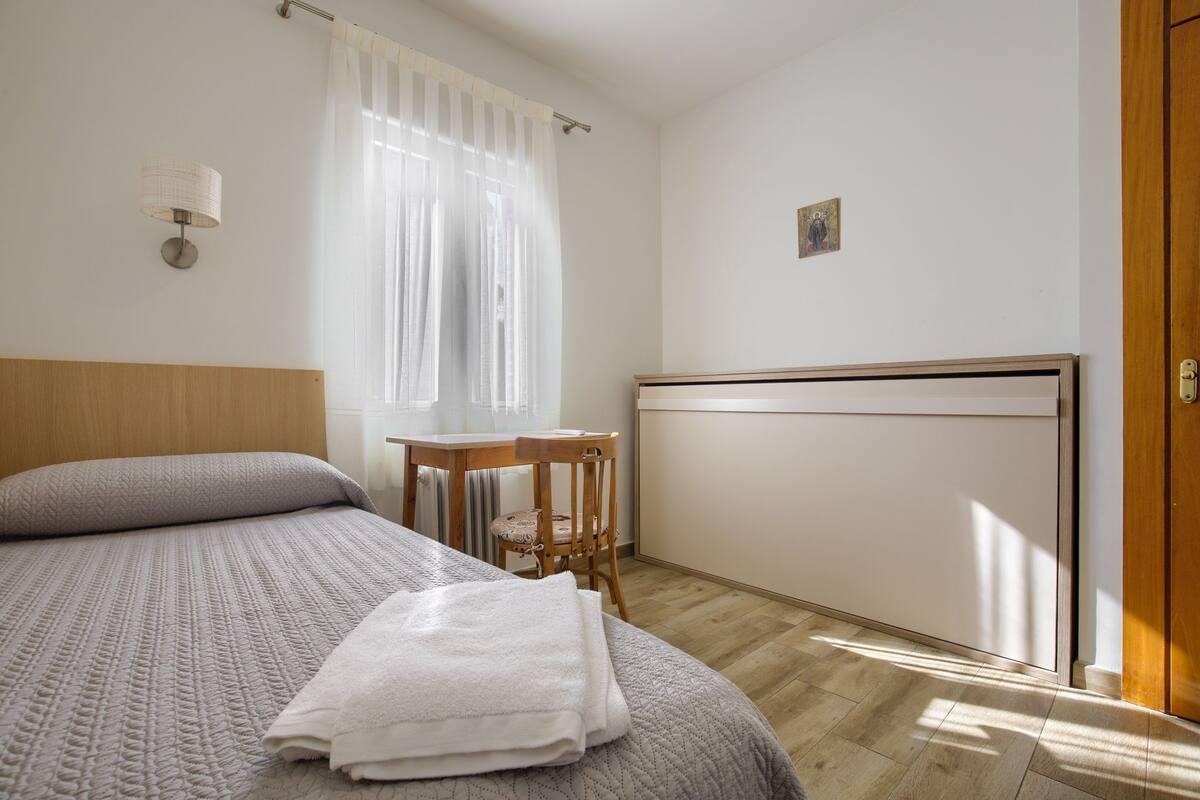 Une chambre à coucher comprenant un lit, une table de chevet, une chaise, une fenêtre avec des rideaux et une porte.