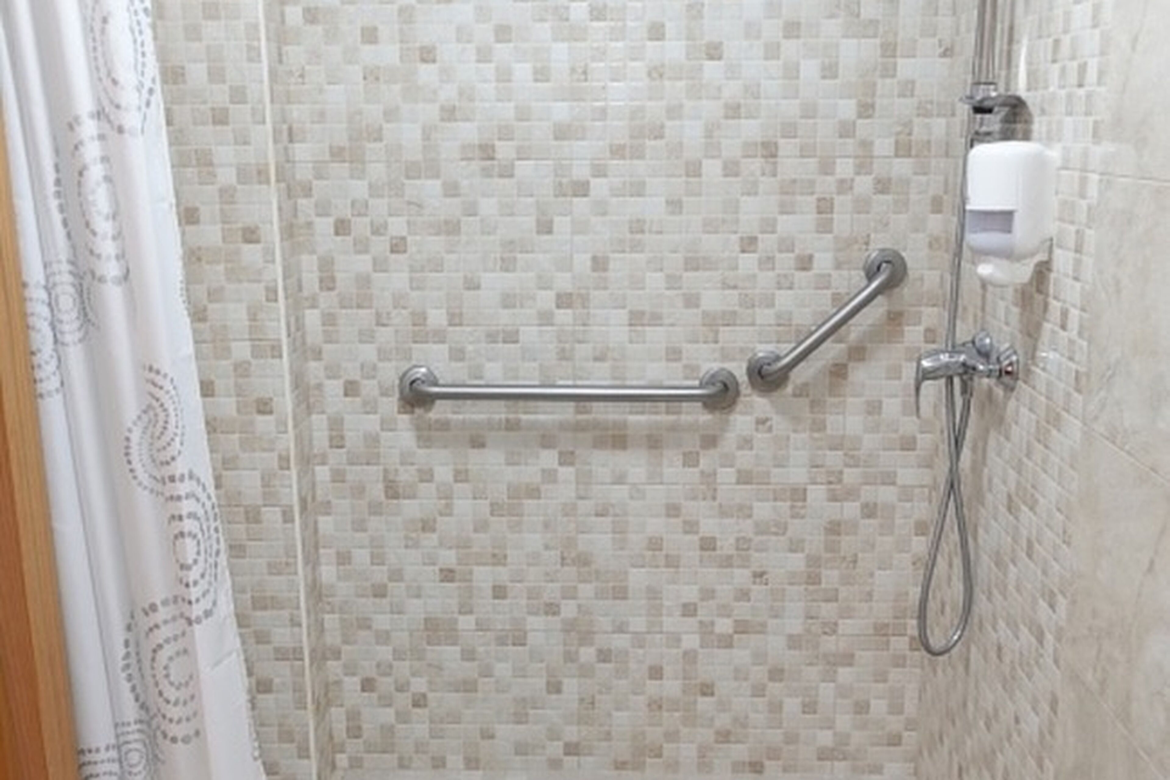 Zona de ducha con pared de azulejos, barra de apoyo y cabezal de ducha manual.