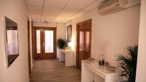 Un corridoio con pavimento in legno, pareti bianche e una reception con una pianta e oggetti decorativi.