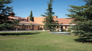 Un edificio con facciata in mattoni e tetto in tegole, circondato da un prato curato e diversi alberi sempreverdi.