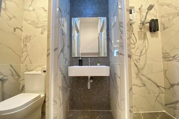 A bathroom with a marble wall, a white sink, a mirror, and a shower. - The Grand SS15 Sunway 4Pax 2 Bedroom (Subang Jaya)