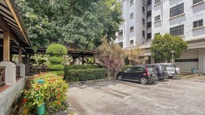 A parking area with a covered structure, a small garden with red flowers, and a multi-story building in the background. - 1 Bedroom Apartment with balcony city view, Melaka Town Centre CBD (Melaka)