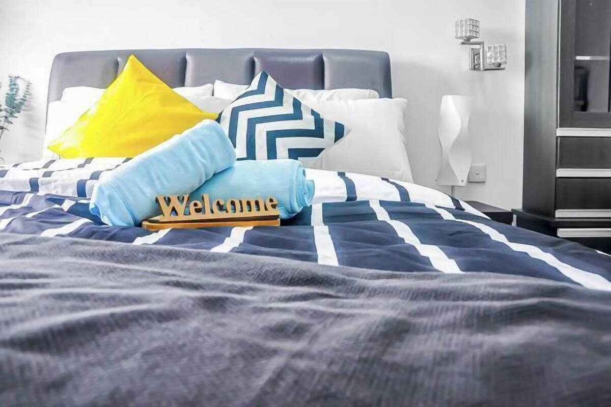 Ein ordentlich gemachtes Bett mit gestreifter Bettwäsche, einem 'Welcome'-Schild und dekorativen Kissen.