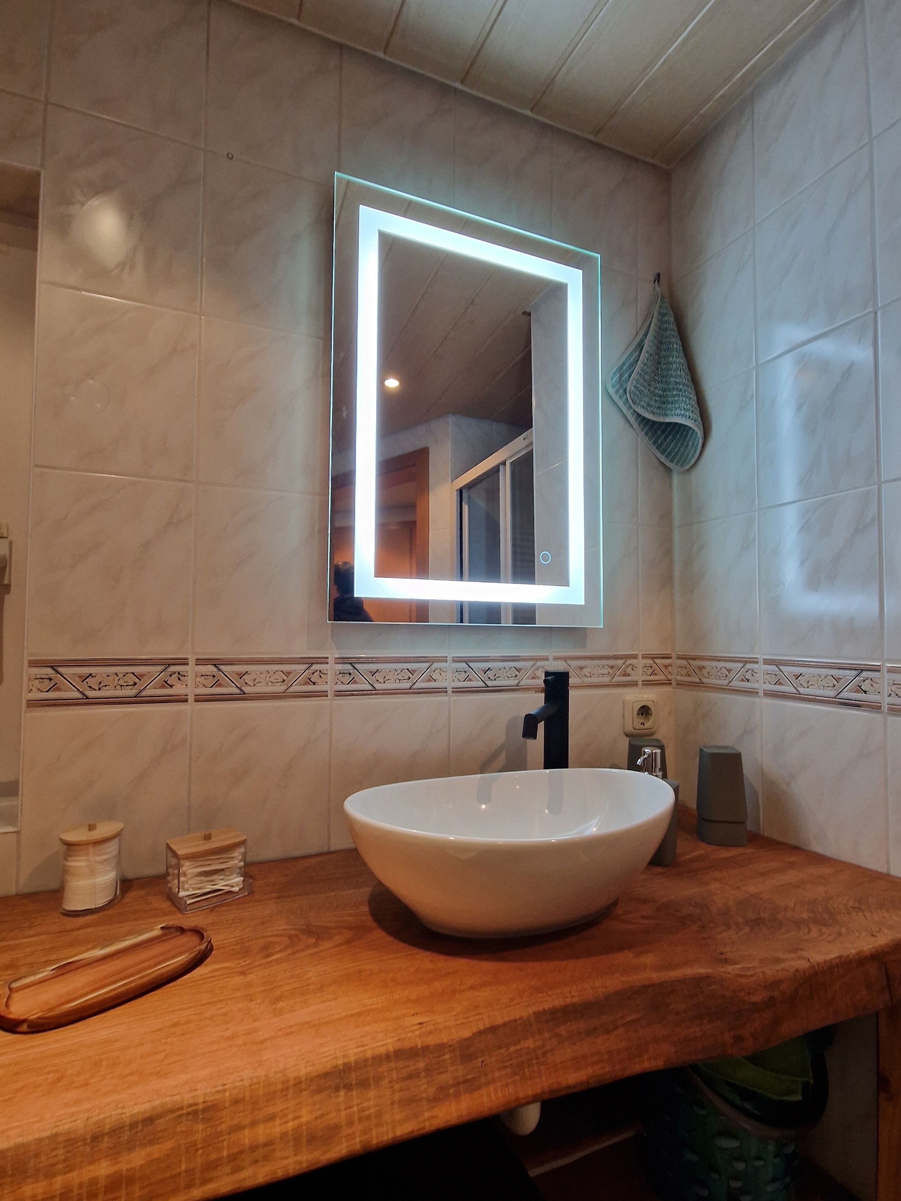 A bathroom with a wooden vanity, a white sink, a mirror with a light, and a towel rack.