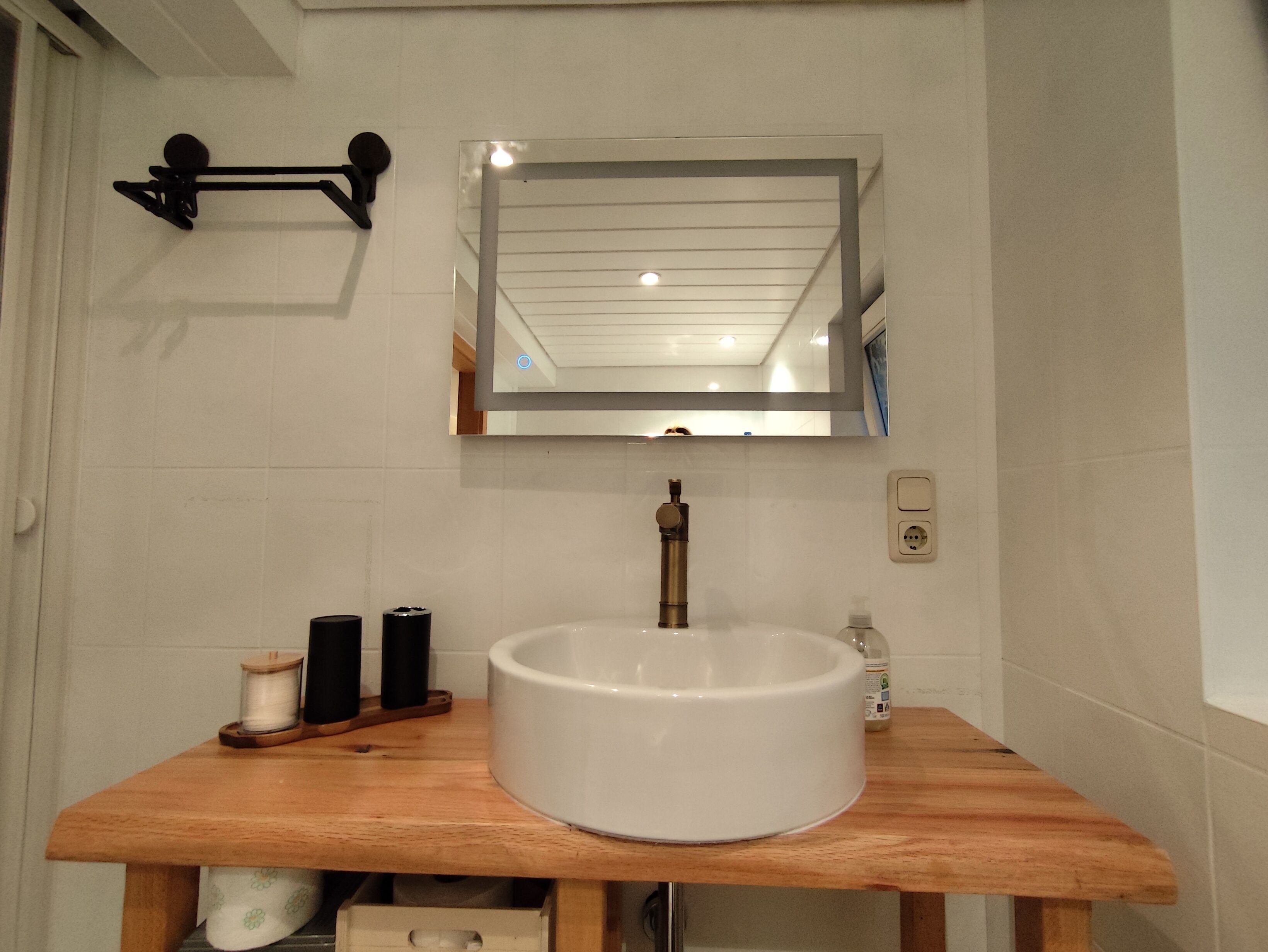 Une salle de bain avec un lavabo blanc, un plan de toilette en bois et un miroir au-dessus.