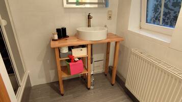 Une salle de bain avec un meuble-lavabo en bois, un lavabo blanc, un miroir et une fenêtre ornée d’un motif floral.