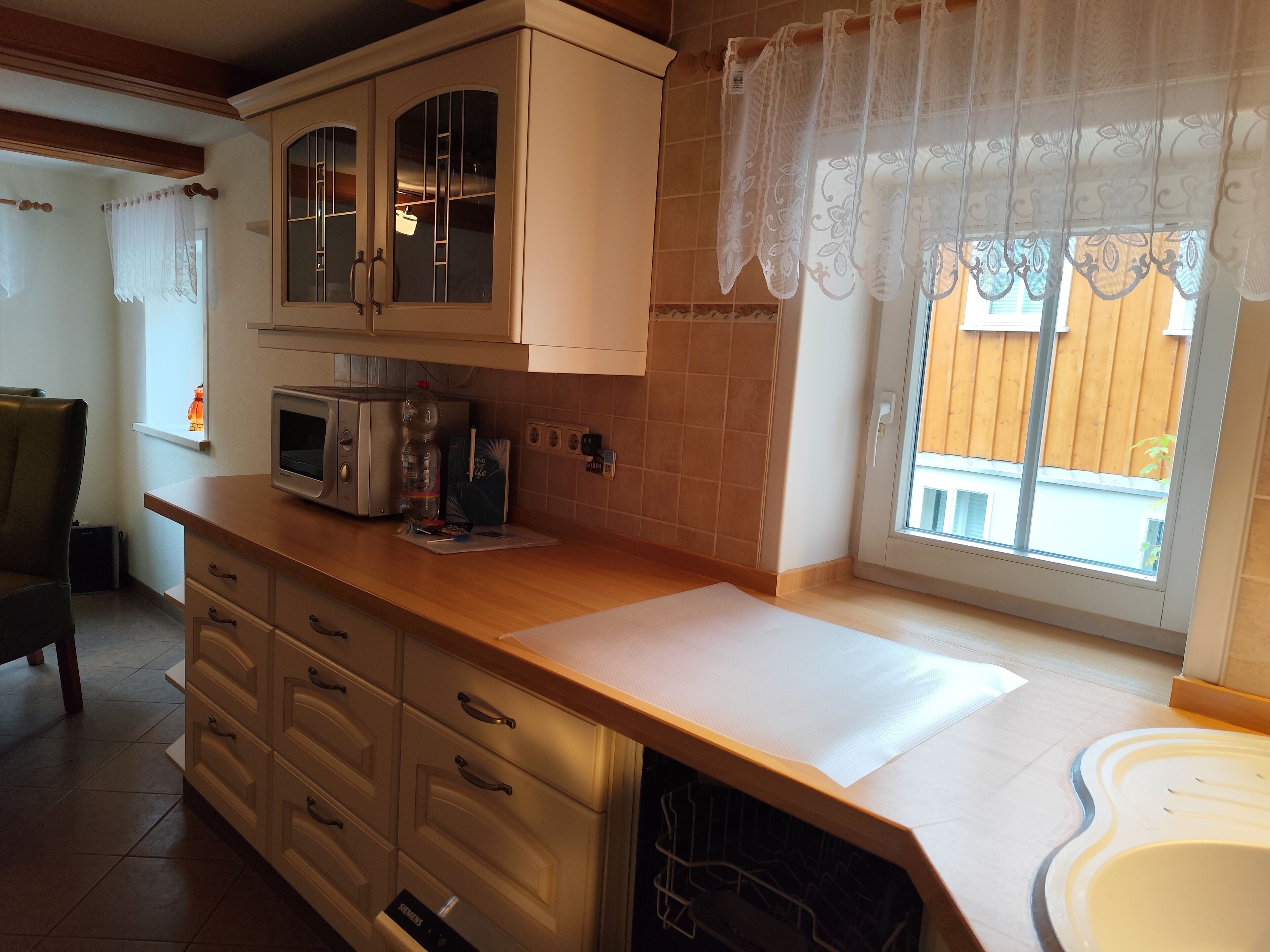 Eine Küche mit Mikrowelle, Toaster und Spüle. Es gibt Schränke und ein Fenster mit Vorhängen.