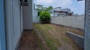 A narrow courtyard with a concrete wall, a small tree, and a building with a window and air conditioning unit. - The Hideout - 2Br Villa Near Kahathuduwa Interchange (Polgasowita)