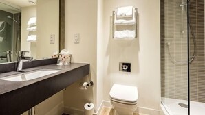 Un baño moderno con un espejo grande, un lavabo, un inodoro y una ducha con mampara de vidrio.