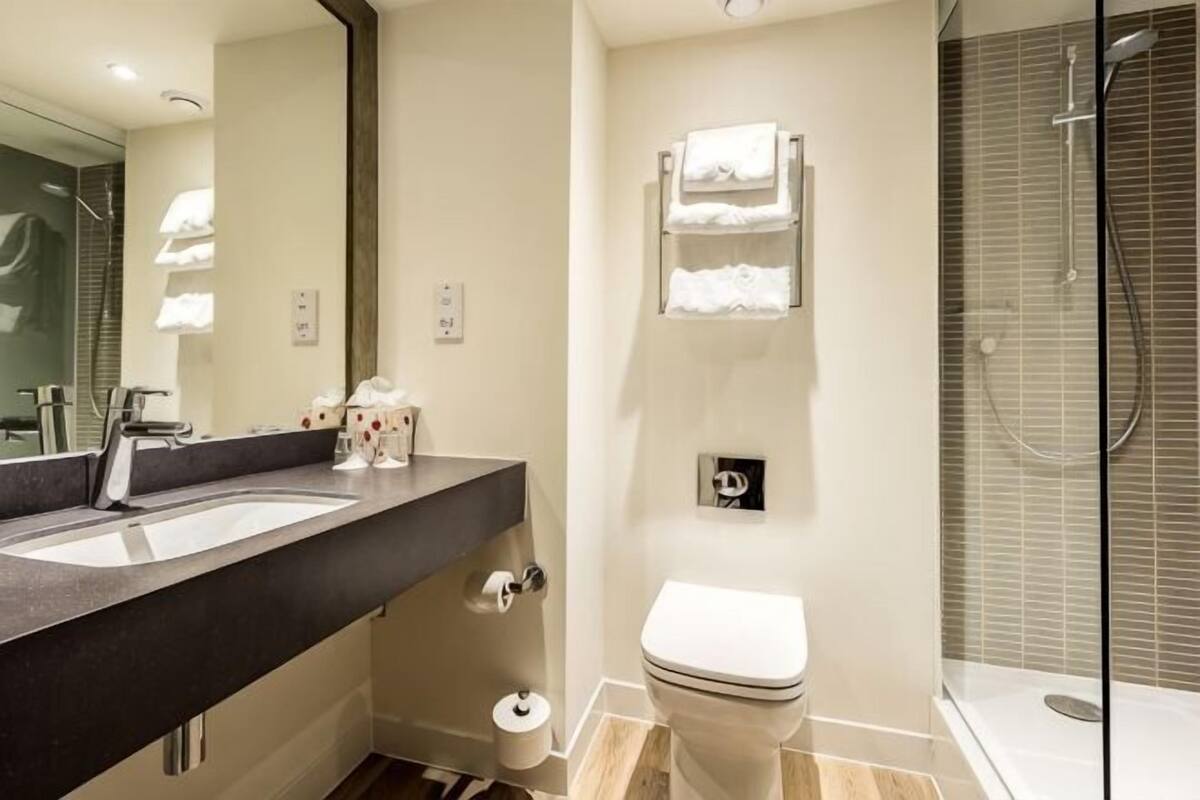 Un baño moderno con un espejo grande, un lavabo, un inodoro y una ducha con mampara de vidrio.