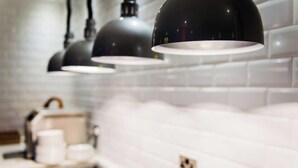 Una cocina con azulejos blancos tipo metro, lámparas colgantes negras y una cafetera.