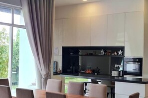 Een moderne keuken met witte kasten, een inbouwoven en een eethoek met een tafel en stoelen.