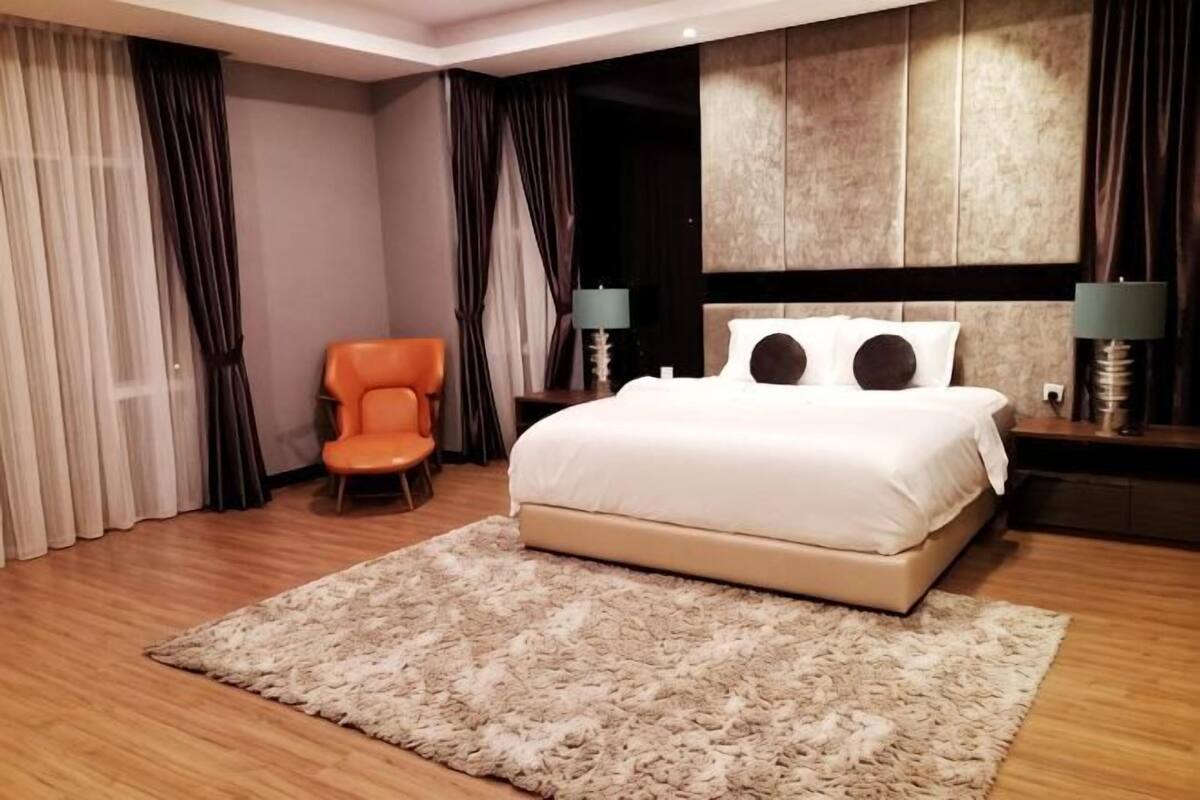 A hotel room with a large bed, a chair, a nightstand, and a wall-mounted headboard.