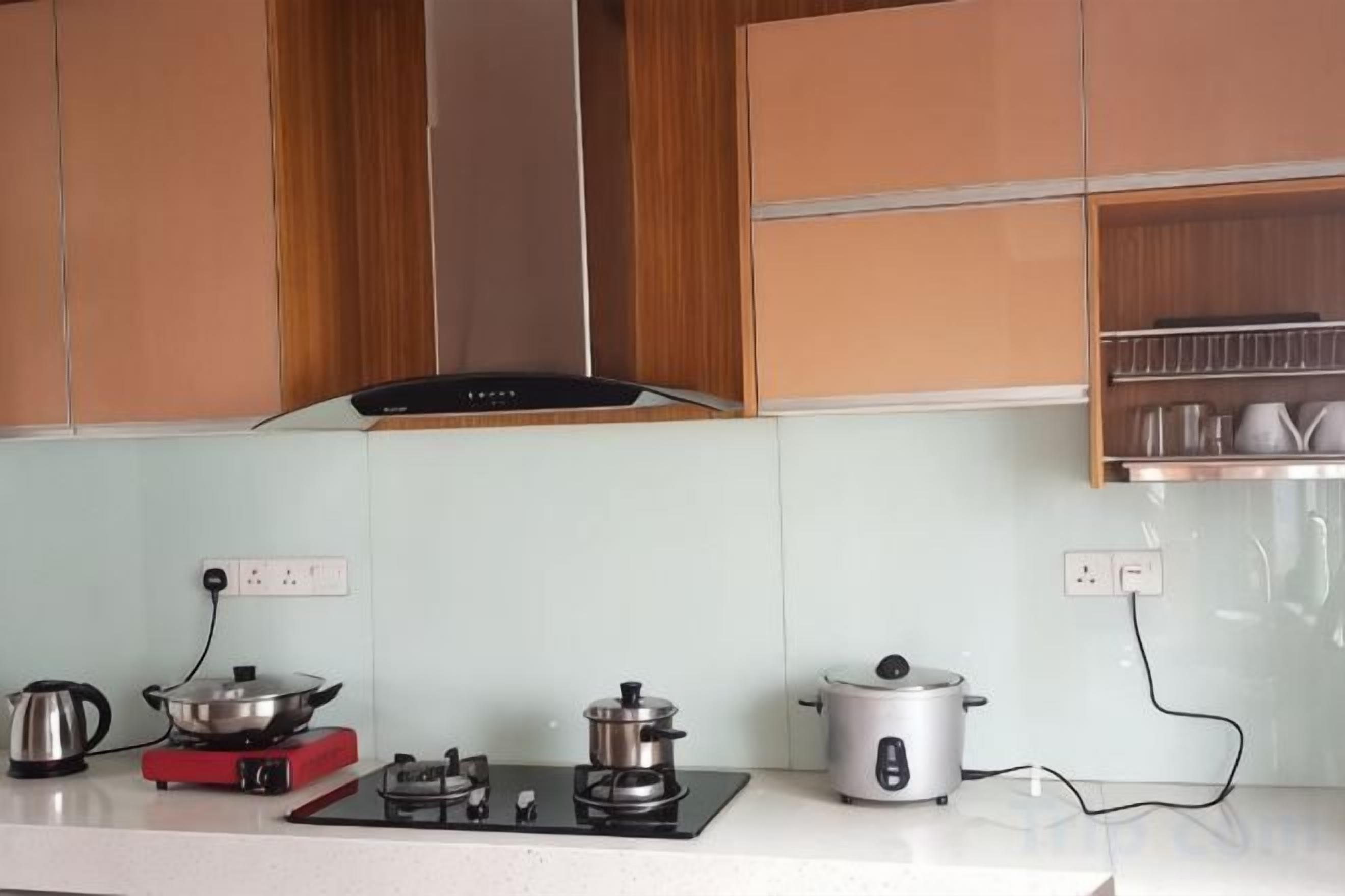 Une cuisine avec des meubles en bois, une cuisinière à gaz, une bouilloire et un cuiseur à riz.