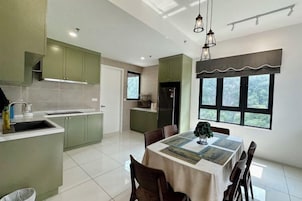 A modern kitchen with green cabinets, a dining area with a table and chairs, and a large window with a view of greenery.