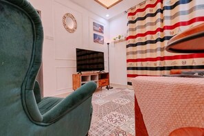 A room with a large green armchair, a flat-screen TV on a wooden stand, a patterned rug, and a striped curtain. - WHITE ON HOMESTAY CAMERON BY ICOLOR (Tanah Rata)