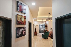 A hallway with artwork on the walls, a staircase, and a dining area with chairs. - WHITE ON HOMESTAY CAMERON BY ICOLOR (Tanah Rata)