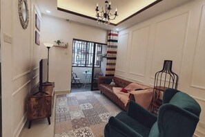 Een woonkamer met een bank, een salontafel, een televisie, een kamerbreed tapijt met een patroon, een kroonluchter en uitzicht door een raam.
