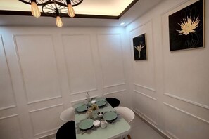 A dining area with a table set for four, white paneled walls, and a ceiling light fixture. - WHITE ON HOMESTAY CAMERON BY ICOLOR (Tanah Rata)