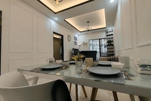 A modern dining area with a glass table, white walls, and a chandelier. - WHITE ON HOMESTAY CAMERON BY ICOLOR (Tanah Rata)