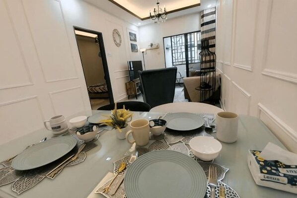 A dining table set with plates, bowls, and cups, with a chair and a vase of flowers. - WHITE ON HOMESTAY CAMERON BY ICOLOR (Tanah Rata)