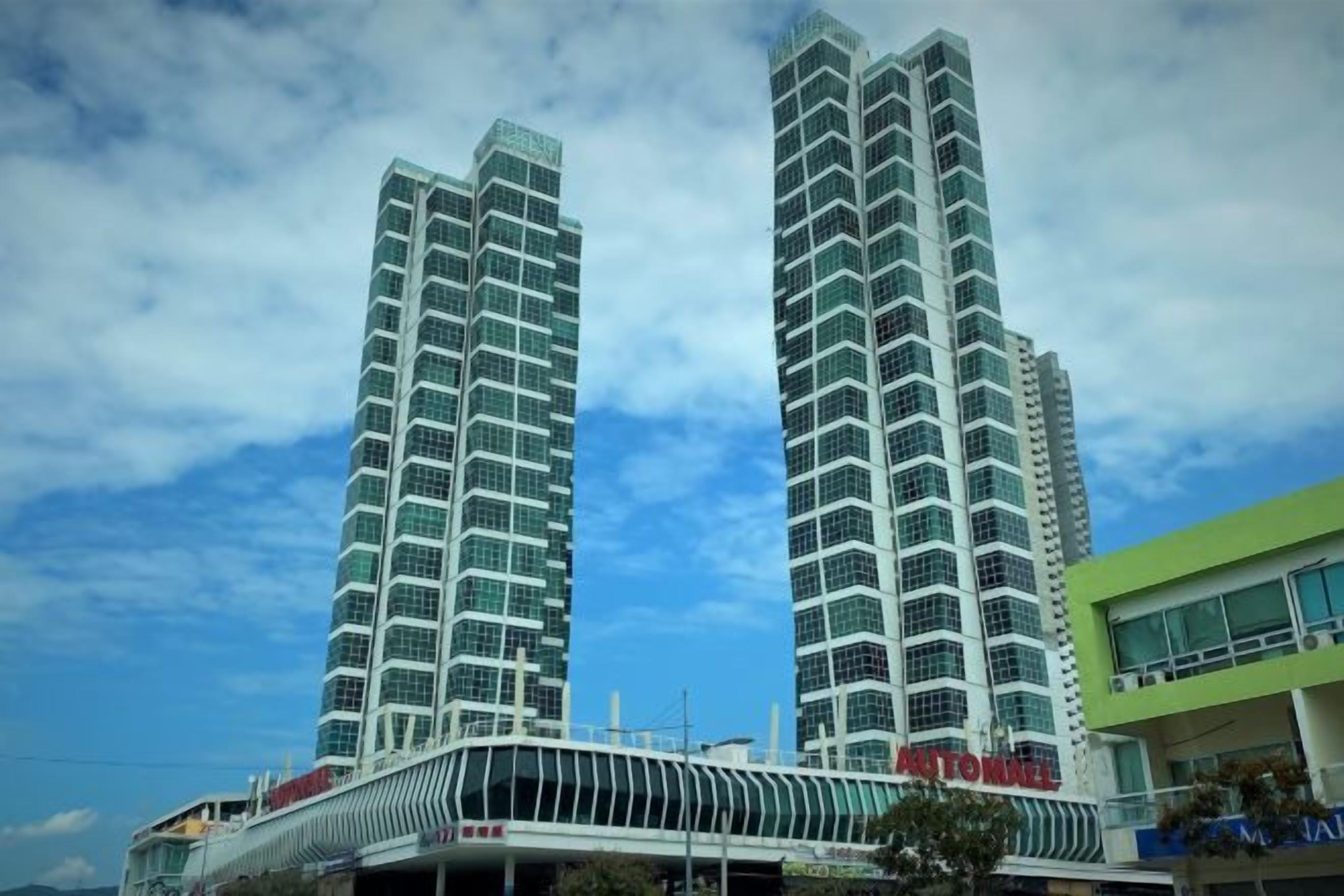 Two high-rise buildings with a modern design, a covered walkway, and a green building with a sign.