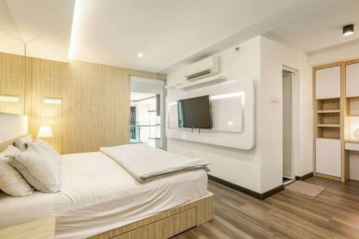 A modern hotel room with a bed, a flat-screen TV, an air conditioning unit, and a wooden floor.