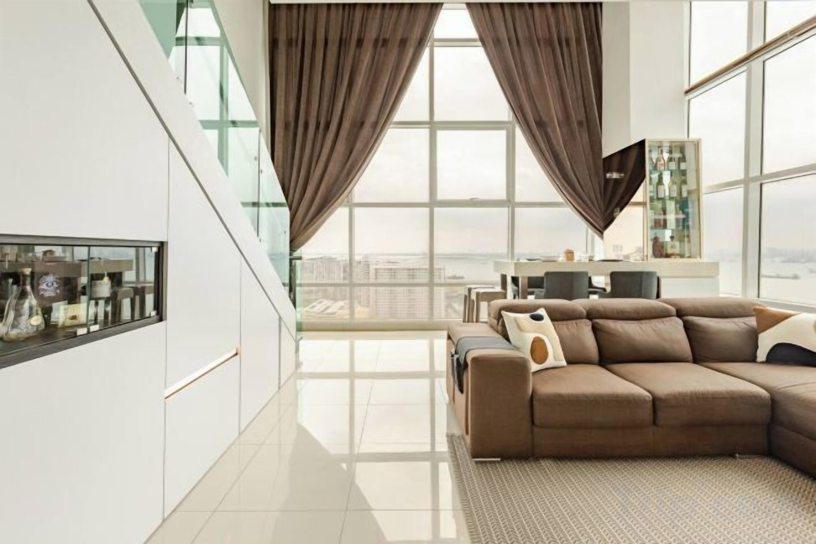 Una sala de estar moderna con un sofá seccional grande, una mesa de centro de vidrio y vistas de la ciudad a través de amplias ventanas.