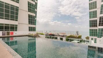 Una piscina infinita en la azotea con vista al mar y edificios.