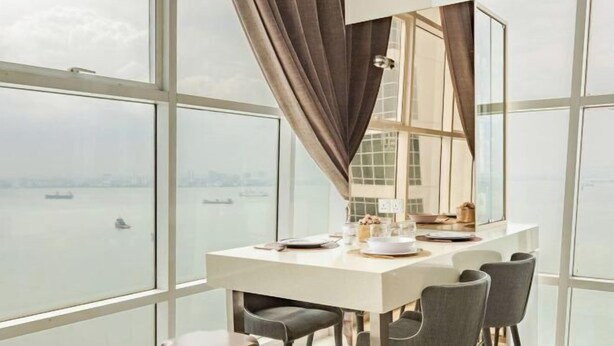 A modern dining area with a large window, a table set for two, and a view of the water. - The Panoramic Duplex Glass Suite @ Karpal Singh Drive Georgetown, Penang. (Jelutong)