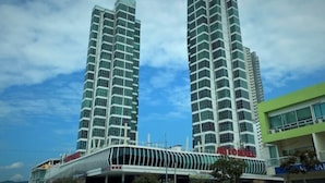 Two tall, modern high-rise buildings with a glass facade, a covered walkway, and a green building with signage. - The Panoramic Duplex Glass Suite @ Karpal Singh Drive Georgetown, Penang. (Jelutong)