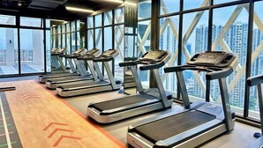 A gym with treadmills aligned in a row, large windows, and a view of high-rise buildings. - R Residence (Phnom Penh)