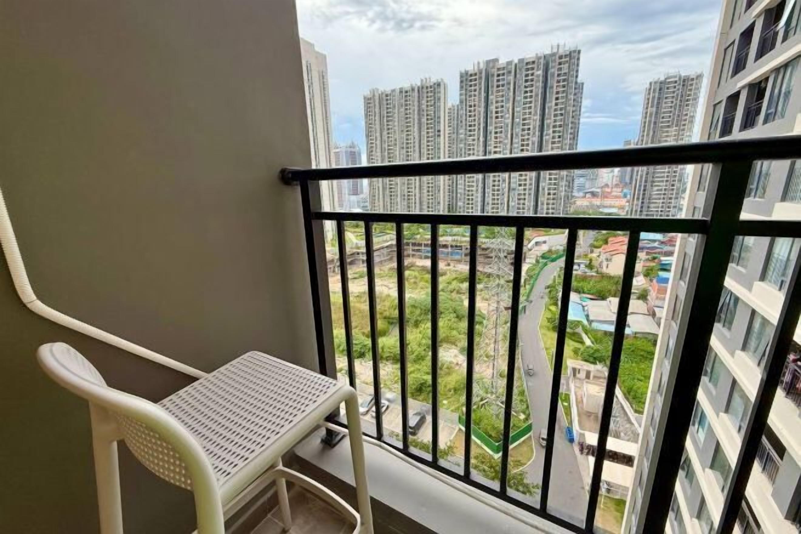A balcony with a white chair, a black railing, and a view of high-rise buildings and greenery below.
