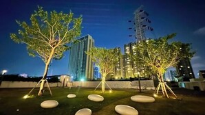 A nighttime view of a landscaped area with trees and illuminated stones, surrounded by high-rise buildings. - R Residence (Phnom Penh)