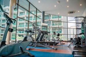 Une salle de sport équipée de machines de cardio, d’appareils de musculation et de grandes fenêtres donnant sur un immeuble.