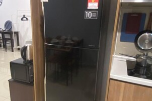 A black refrigerator with a digital display, a microwave, and a kettle on a countertop.