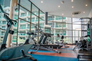 A gym with cardio equipment, weight machines, and a large window overlooking a building.