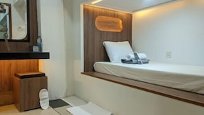 Une petite chambre moderne, équipée d’un lit, d’une tête de lit en bois, d’un miroir et d’une petite armoire en bois.