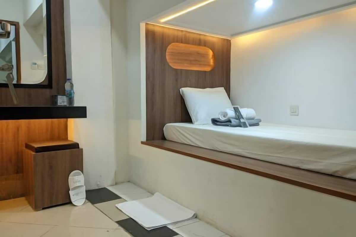 A small, modern room with a bed, a wooden headboard, a mirror, and a small wooden cabinet.
