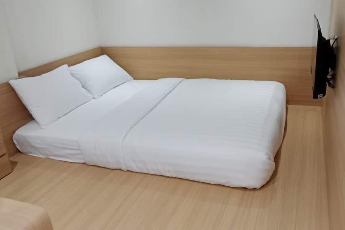 A single bed with white bedding in a room with light wooden flooring and a wooden headboard.