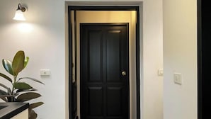 A hallway with a dark door, a wall-mounted light fixture, and a potted plant. - Luxury Thai Design Home – Chinatown Self Check In (Bangkok)