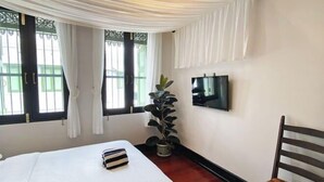 A bedroom with a bed, a potted plant, a TV on the wall, and a window with curtains. - Luxury Thai Design Home – Chinatown Self Check In (Bangkok)