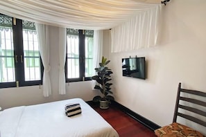 A bedroom with a bed, a potted plant, a TV on the wall, and a window with curtains. - Luxury Thai Design Home – Chinatown Self Check In (Bangkok)