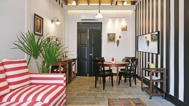 A cozy living area with a striped sofa, a dining table with chairs, a potted plant, and a black-framed picture on the wall. - Luxury Thai Design Home – Chinatown Self Check In (Bangkok)