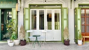 A building entrance with a green awning, a glass door with white shutters, and potted plants. - Luxury Thai Design Home – Chinatown Self Check In (Bangkok)