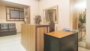 A reception area with a wooden reception desk, a leather sofa, a mirror, and a potted plant. - Kababayan Pensione House by RedDoorz (Iloilo City)