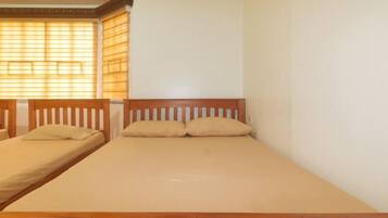 A single bed with a wooden headboard and two pillows, a window with blinds, and a plain wall.